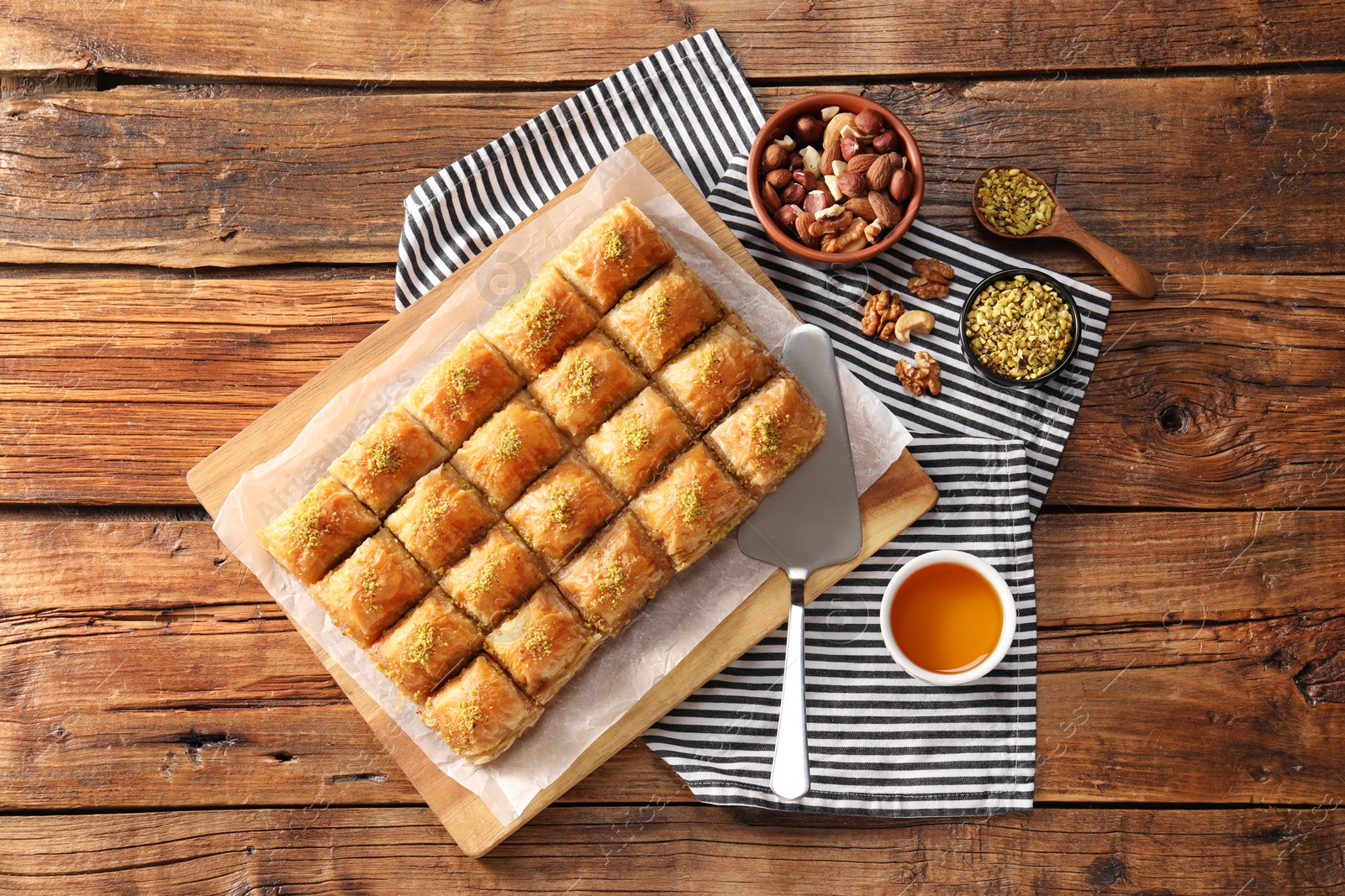 Photo of Delicious sweet baklava with ingredients and cake server on wooden table, flat lay