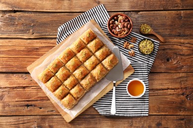 Photo of Delicious sweet baklava with ingredients and cake server on wooden table, flat lay