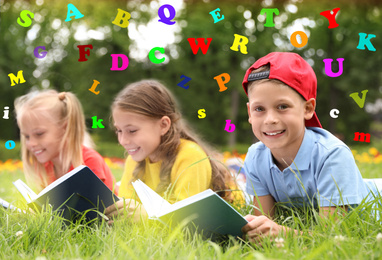 Group of little children reading books on green grass in park