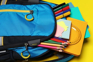 Backpack with school stationery on yellow background, closeup