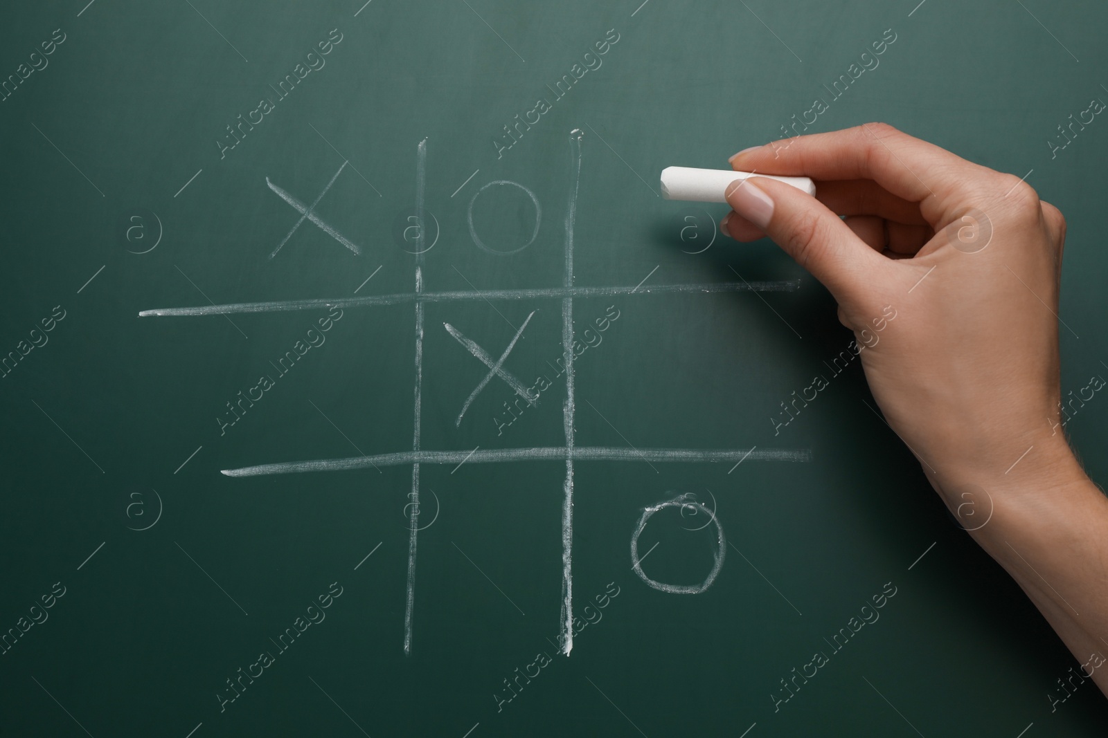 Photo of Woman playing tic tac toe game on green chalkboard, top view