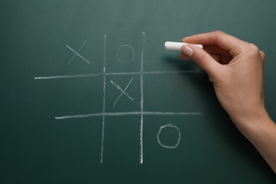 Photo of Woman playing tic tac toe game on green chalkboard, top view