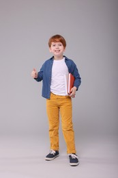 Photo of Happy schoolboy with books showing thumb up on grey background