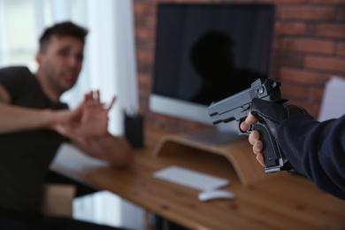 Photo of Man aiming his victim with gun indoors, closeup. Dangerous criminal