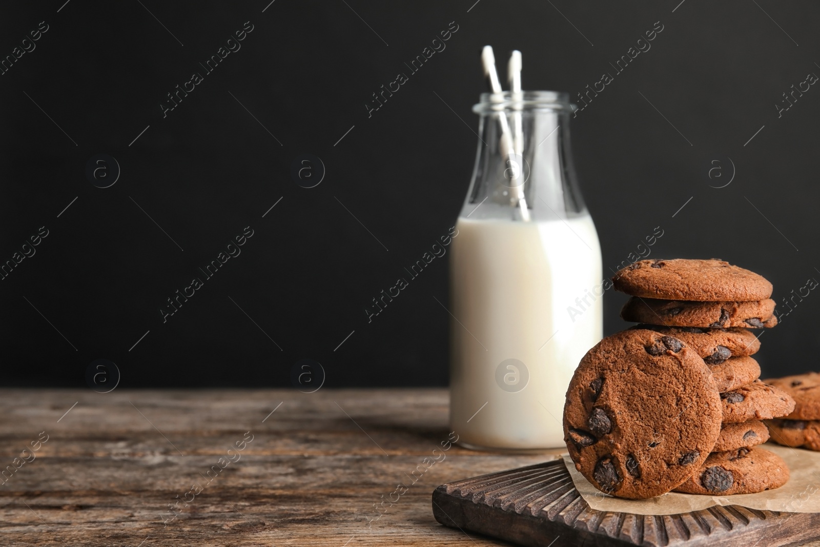 Photo of Tasty chocolate chip cookies and bottle of milk on wooden table. Space for text