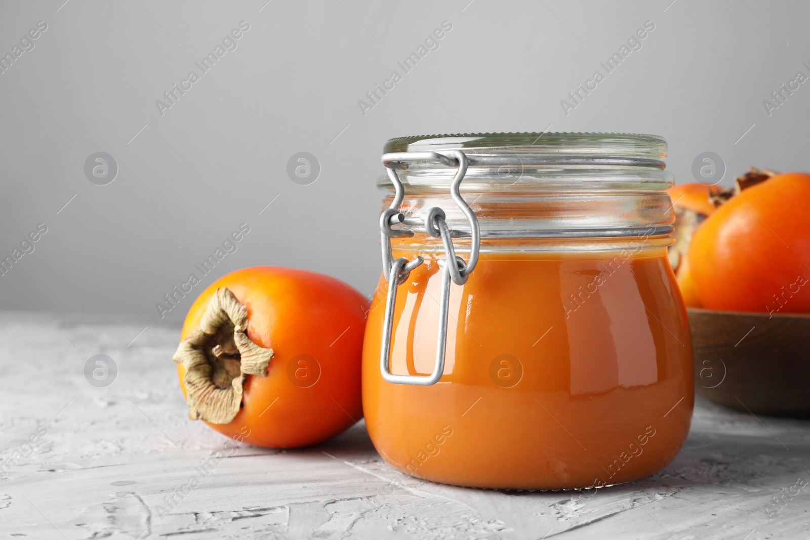 Photo of Delicious persimmon jam and fresh fruits on grey table