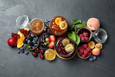 Photo of Jars with different jams and fresh fruits on black table, flat lay