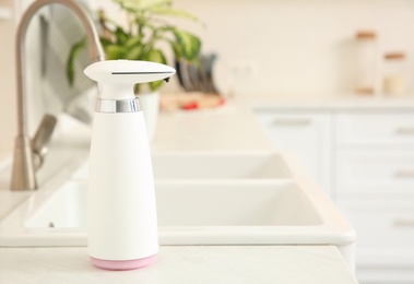 Modern automatic soap dispenser on countertop in kitchen. Space for text