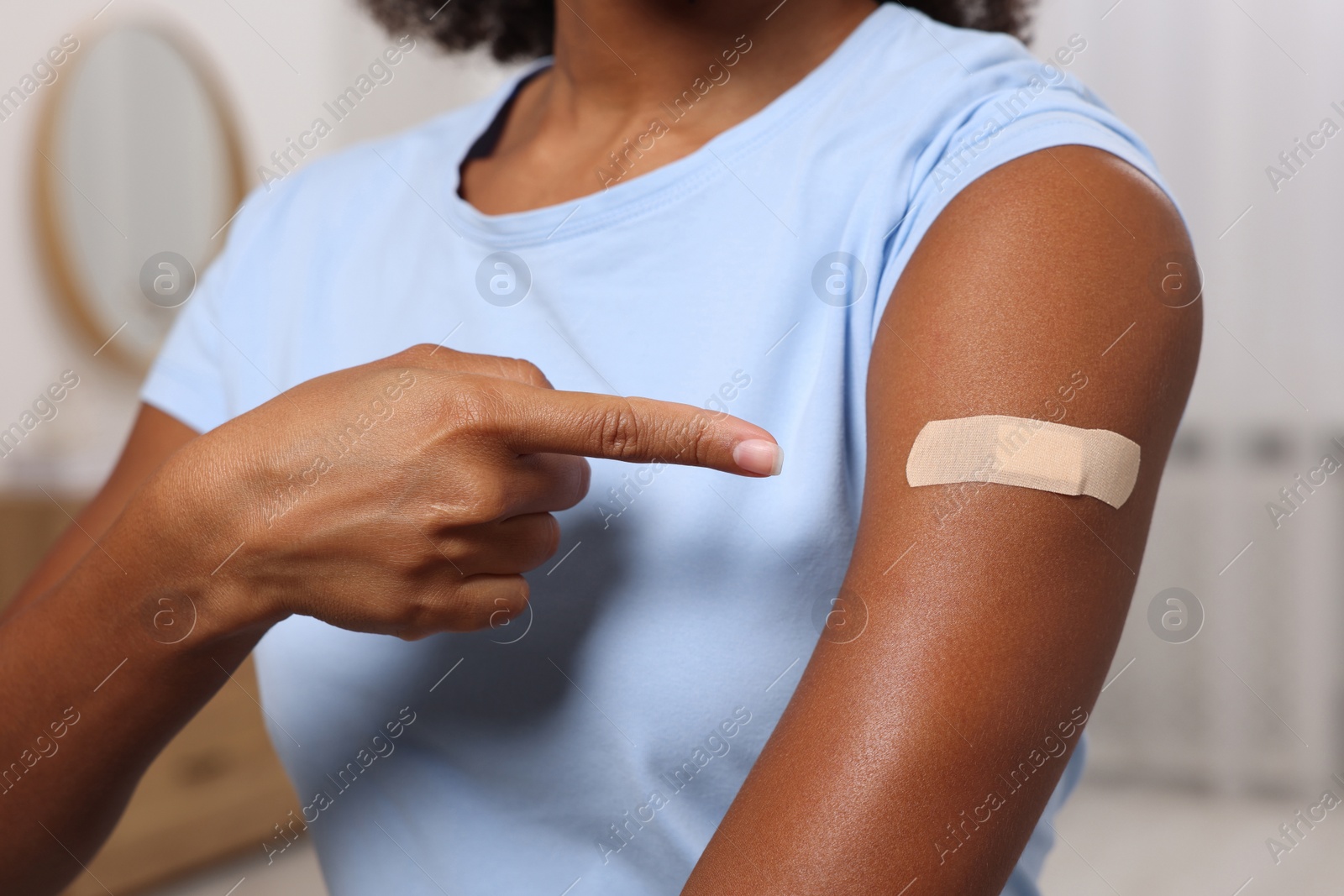 Photo of Young woman pointing at adhesive bandage after vaccination indoors, closeup