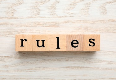 Photo of Word Rules made of cubes with letters on light wooden table, top view