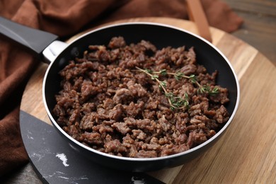 Photo of Fried ground meat and thyme in frying pan on wooden table, closeup