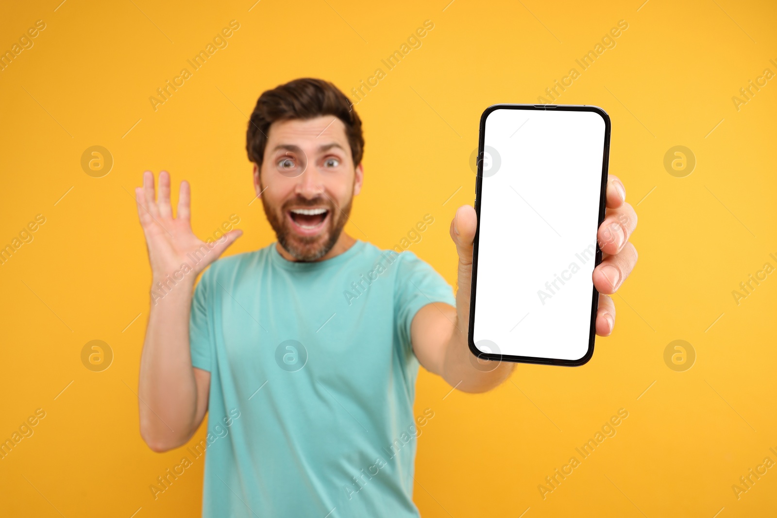 Photo of Surprised man showing smartphone in hand on yellow background, selective focus. Mockup for design