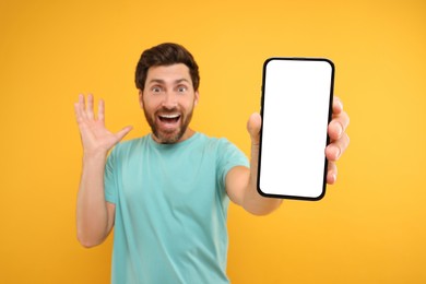 Photo of Surprised man showing smartphone in hand on yellow background, selective focus. Mockup for design