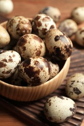 Photo of Bowl and many speckled quail eggs on table, closeup