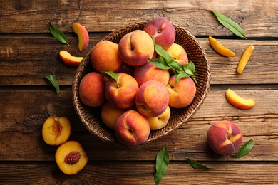 Fresh sweet peaches in wicker basket on wooden table, flat lay