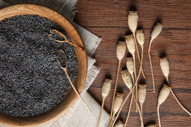 Dry poppy heads and plate with seeds on wooden background, top view