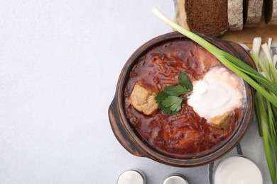 Photo of Tasty borscht with sour cream in bowl served with green onion on light grey table, flat lay. Space for text