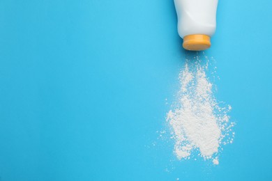 Photo of Bottle and scattered dusting powder on light blue background, top view with space for text. Baby cosmetic product