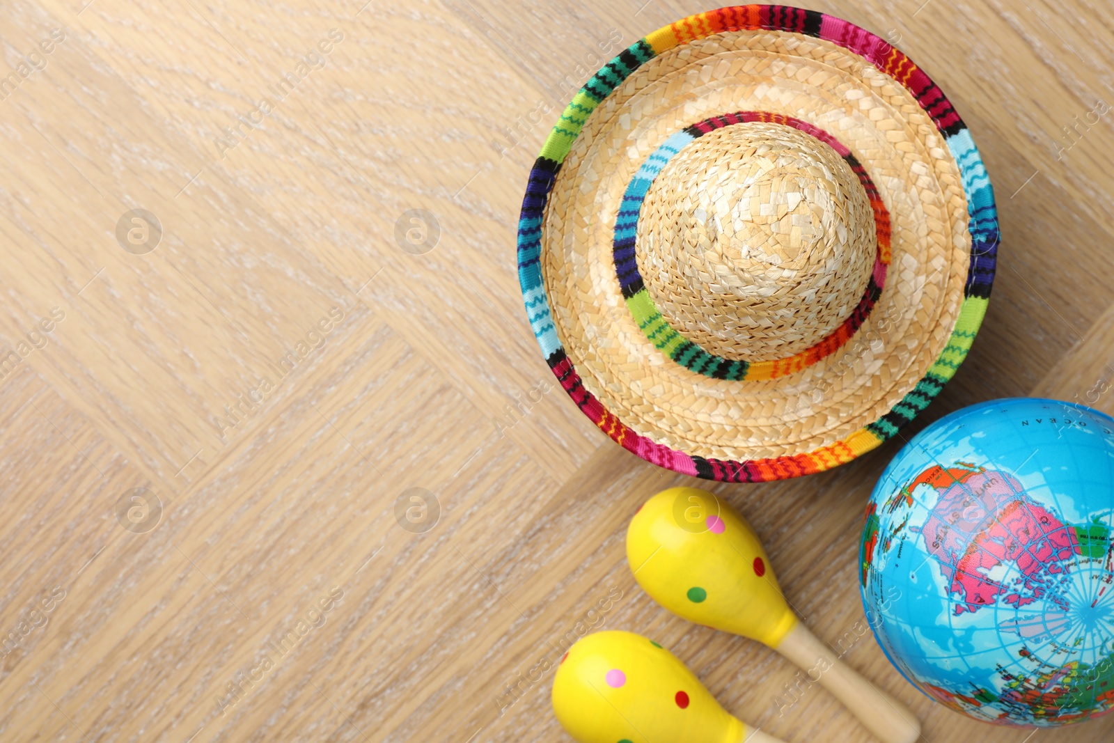 Photo of Mexican sombrero hat, globe and maracas on wooden table, flat lay. Space for text