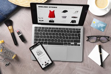 Online store website on laptop screen. Computer, smartphone, coffee and different items on grey table, flat lay