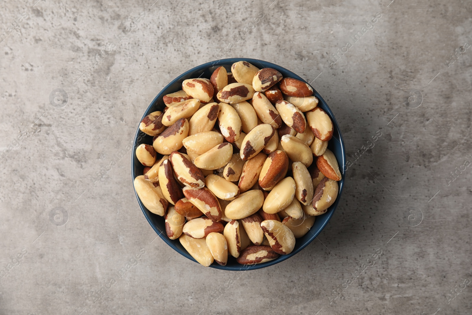 Photo of Bowl with tasty Brazil nuts on grey background, top view