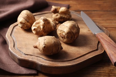 Photo of Fresh Jerusalem artichokes, cutting board and knife on wooden table, closeup