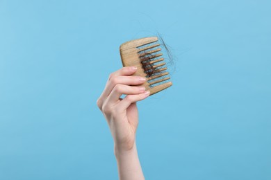 Photo of Woman holding comb with lost hair on light blue background, closeup. Alopecia problem