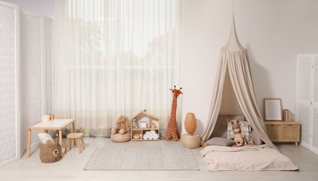 Photo of Cozy kids room with play tent, toys and comfortable floor bed. Montessori interior