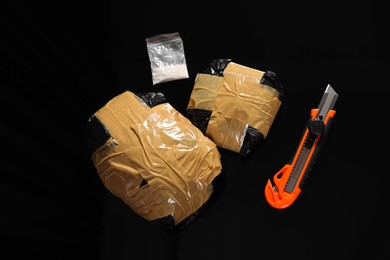 Photo of Smuggling, drug trafficking. Packages with narcotics and utility knife on black surface, flat lay