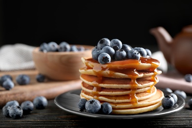 Delicious pancakes with fresh blueberries and caramel syrup on black wooden table