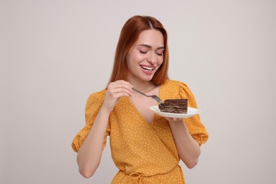 Photo of Young woman eating piece of tasty cake on light grey background