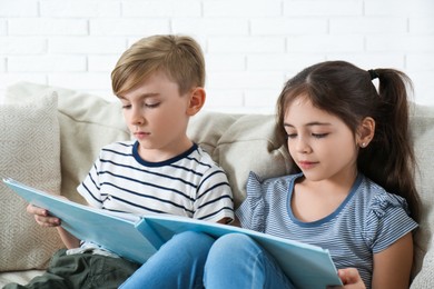 Photo of Little boy and girl reading book on sofa at home