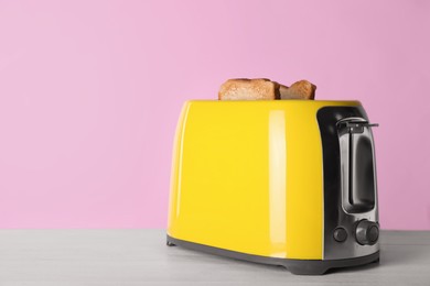 Photo of Modern toaster with slices of roasted bread on white wooden table. Space for text