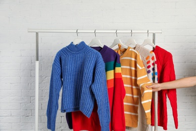 Woman choosing sweater on rack against brick wall