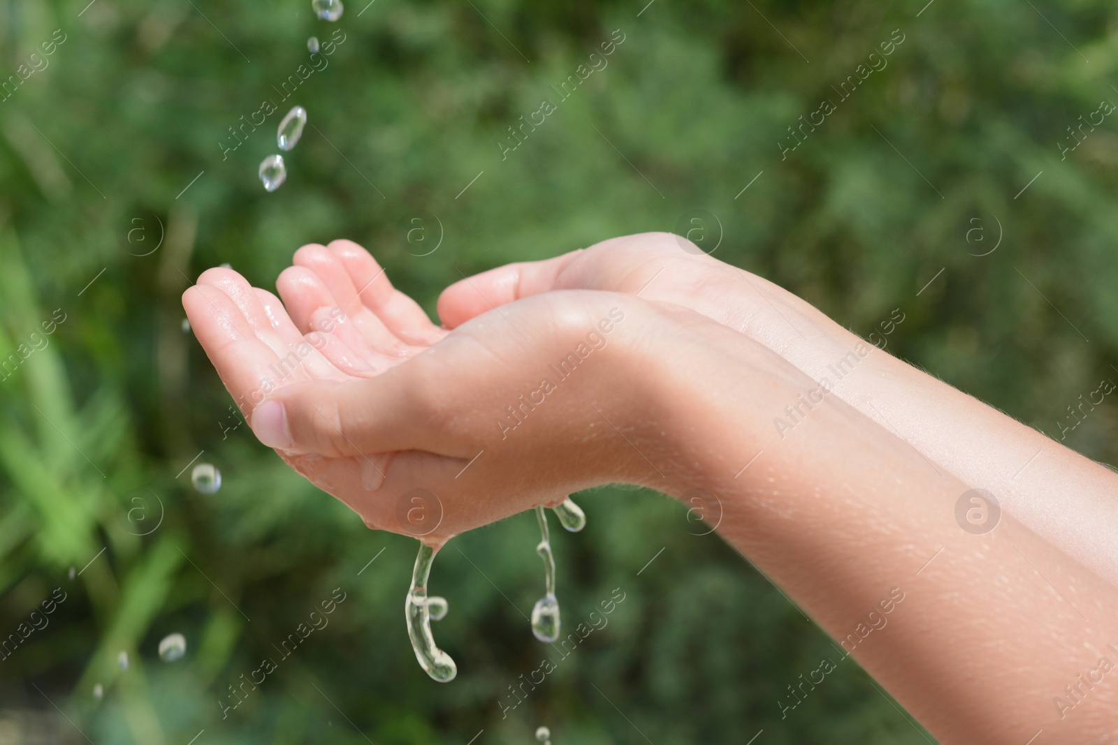 Photo of Pouring water into kid`s hands outdoors, closeup