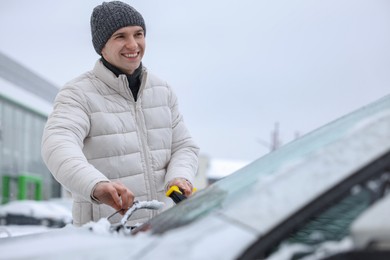 Man cleaning snow from car windshield outdoors, space for text