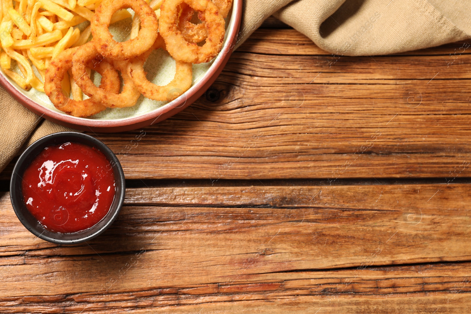 Photo of Tasty fried onion rings and french fries with ketchup on wooden table, flat lay. Space for text