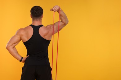 Photo of Young man exercising with elastic resistance band on orange background, back view. Space for text