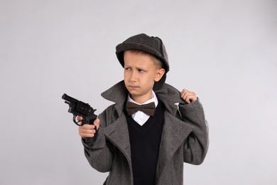 Cute little detective with revolver on grey background