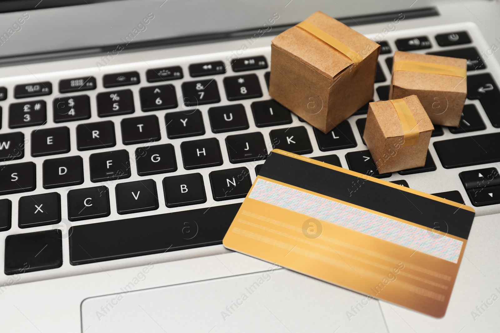 Photo of Internet shopping. Small cardboard boxes and credit card on laptop, closeup. Space for text