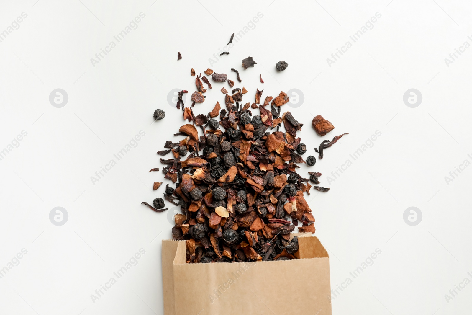 Photo of Paper bag with scattered dried tea on white background, top view