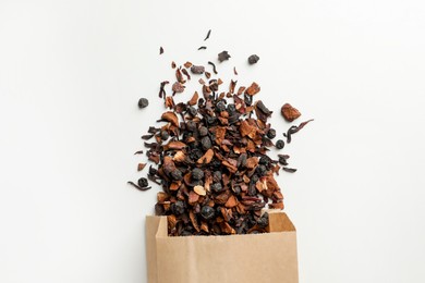 Photo of Paper bag with scattered dried tea on white background, top view