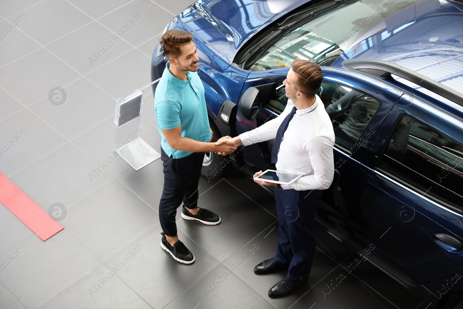 Photo of Young car salesman shaking hands with client in dealership