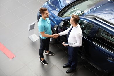 Photo of Young car salesman shaking hands with client in dealership