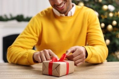 Man opening Christmas gift at wooden table indoors, closeup