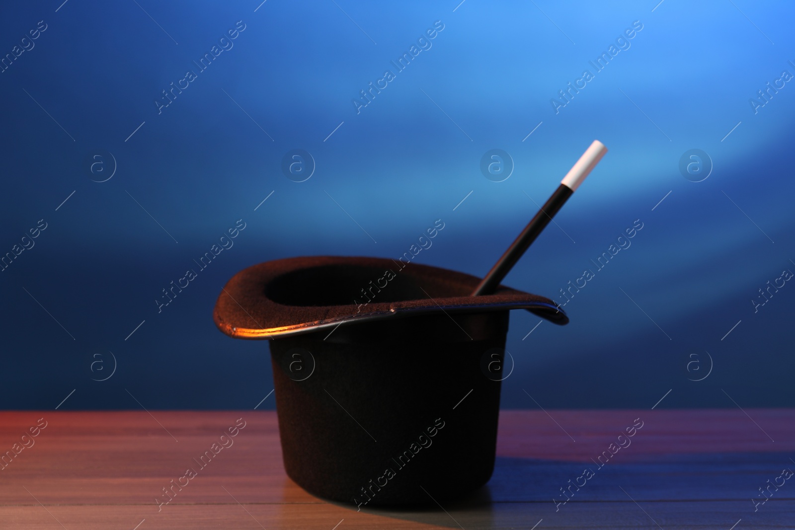 Photo of Magician's hat and wand on wooden table against blue background