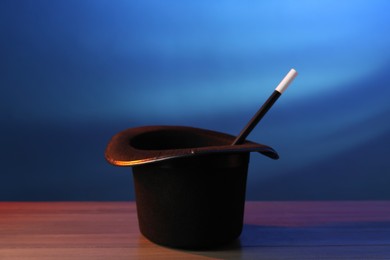 Photo of Magician's hat and wand on wooden table against blue background