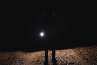 Photo of Silhouette of man with bright flashlight in forest at night