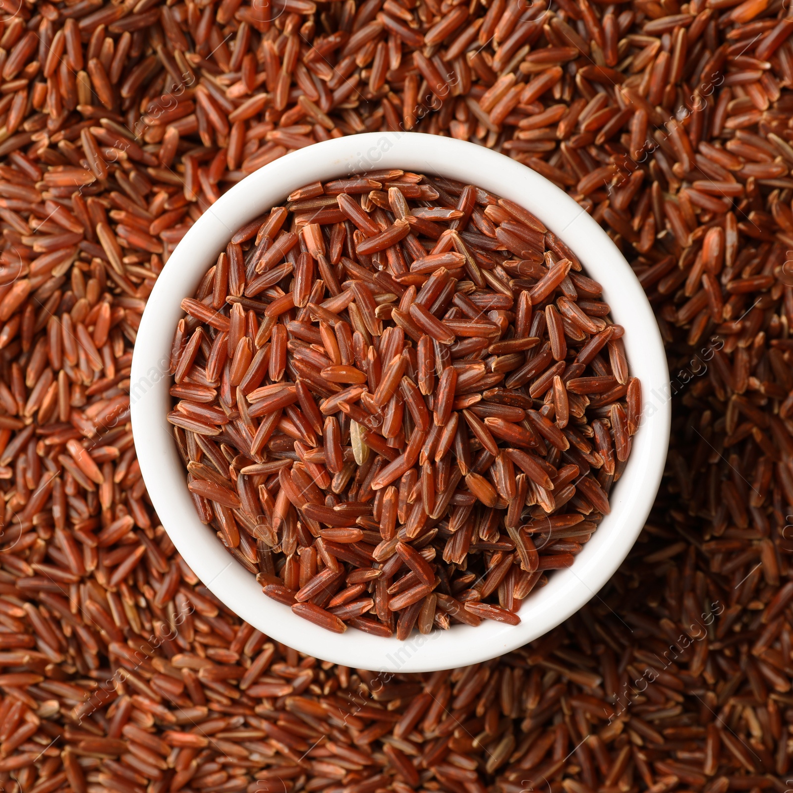 Photo of Ceramic bowl with raw brown rice on cereal, top view