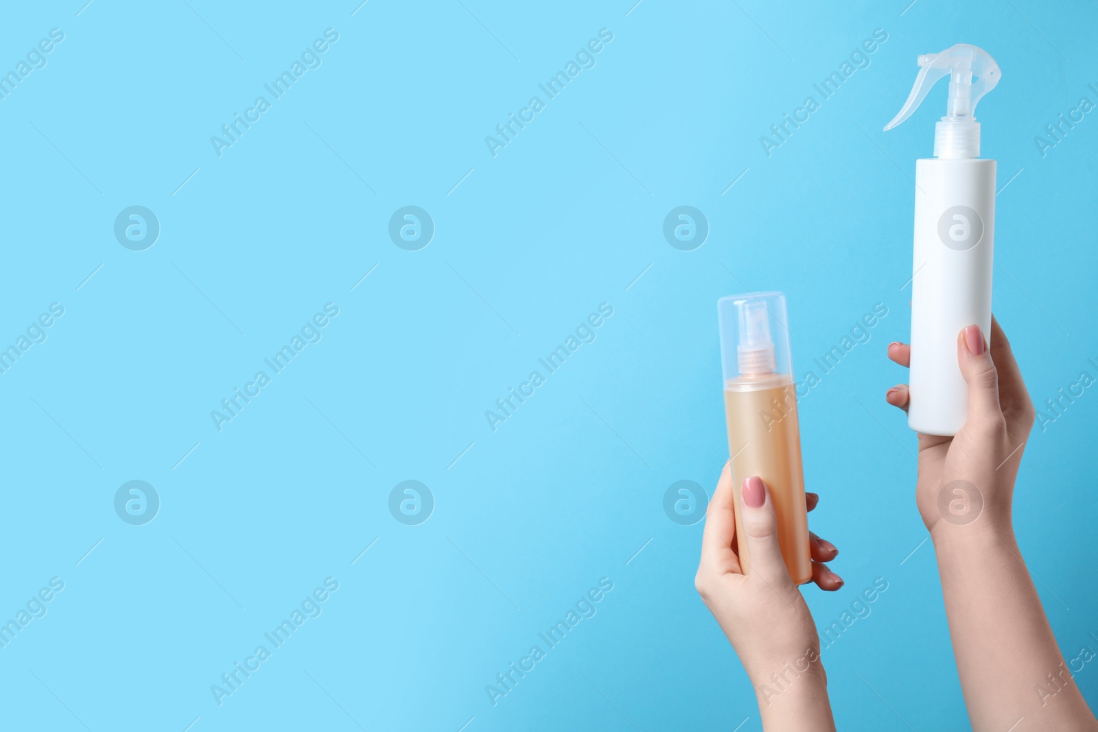 Photo of Woman holding spray bottles with thermal protection on light blue background, closeup. Space for text